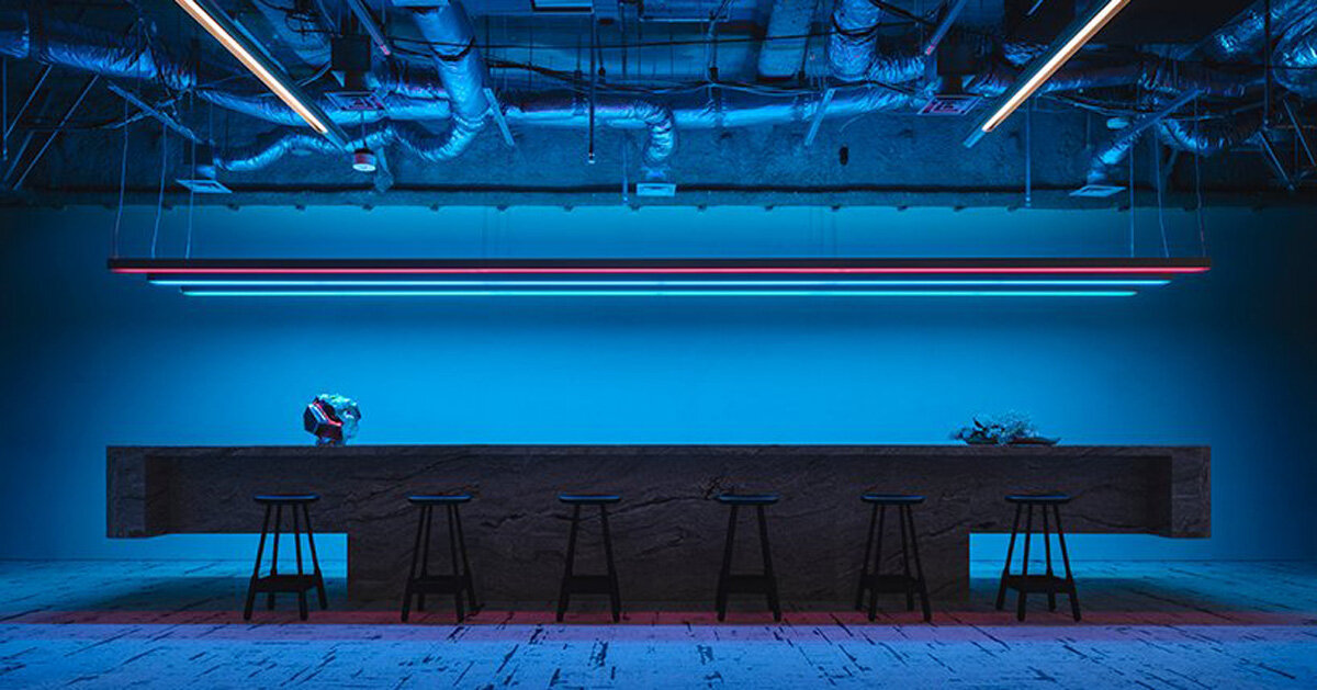 A long stone bar with black stools under blue and red light, in a modern office
